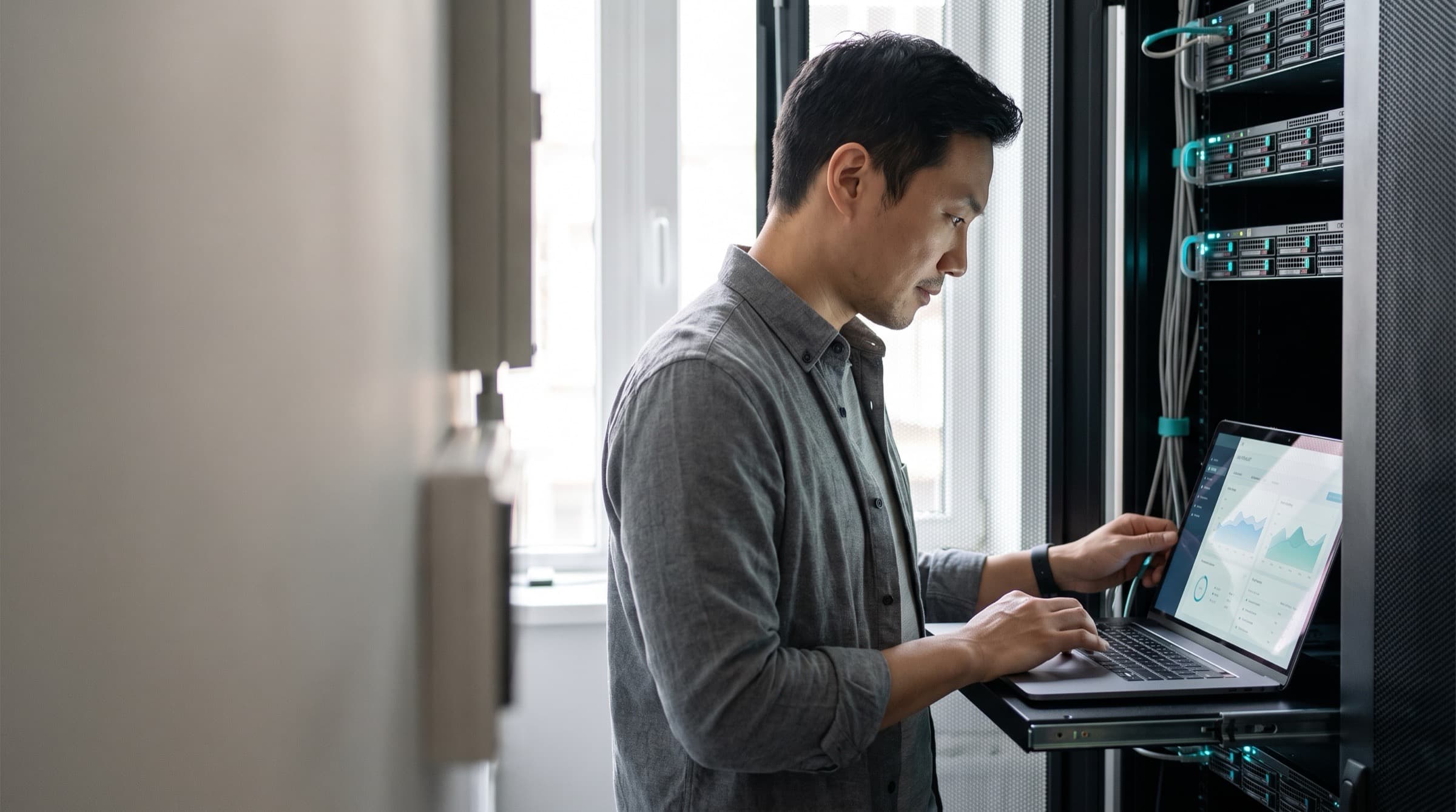 An IT managed service provider owner works on a laptop in a small server room